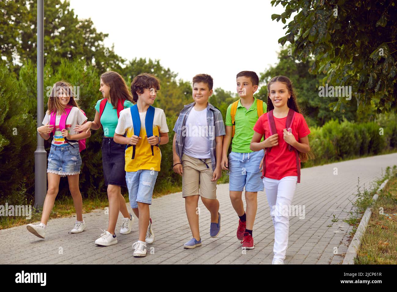 Groupe de petits garçons heureux et de filles parlant tout en marchant à l'école tous ensemble Banque D'Images