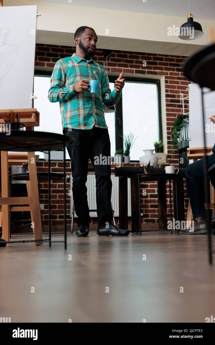 Homme enseignant enseignant aux élèves la technique de l'illustration graphique pendant la leçon d'art en studio de créativité. Équipe multiethnique dessin vase croquis sur toile blanche apprentissage de nouvelles compétences d'esquisse Banque D'Images