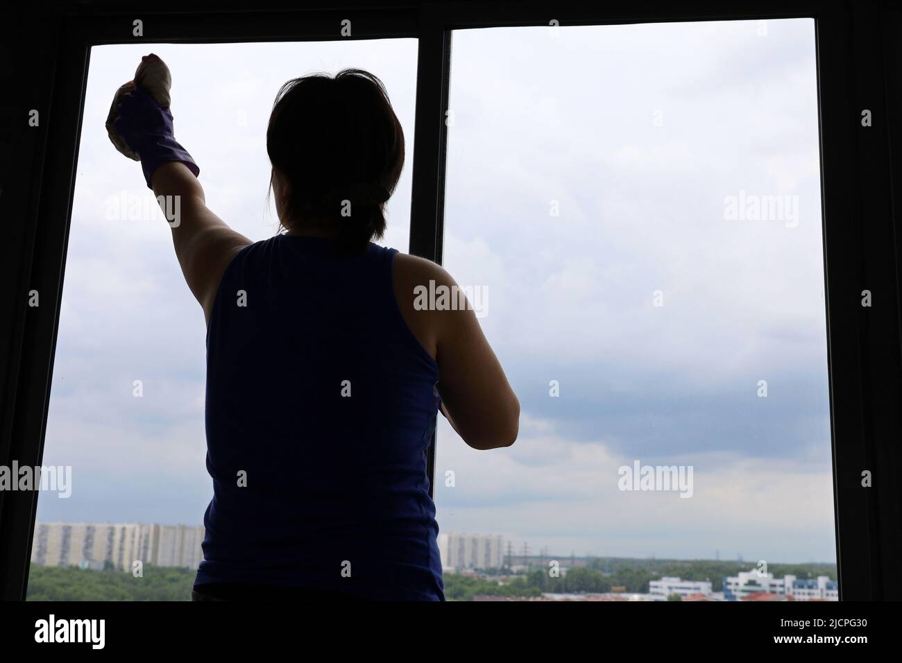 Nettoyage de fenêtres, silhouette d'une femme qui lave le verre, vue intérieure sur la ville d'été Banque D'Images