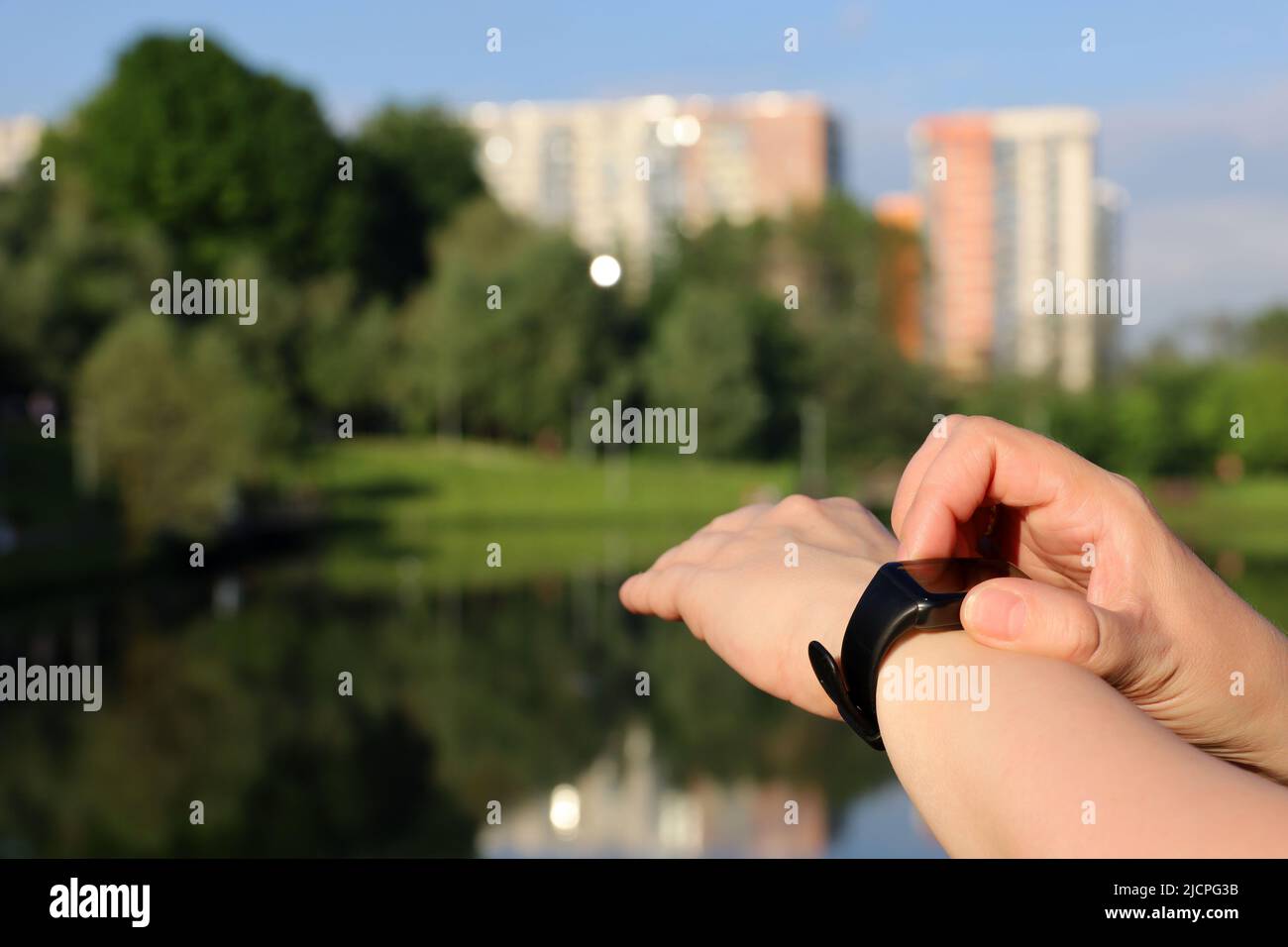 Femme contrôlant le nombre d'étapes et mesurant l'impulsion sur l'affichage de bande intelligente. Les mains des femmes se rapprochent sur le fond du lac dans le parc d'été Banque D'Images