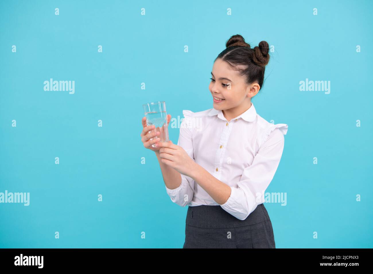 Une jeune fille adorable boit de l'eau en verre sur fond bleu. Bonne adolescente, émotions positives et souriantes de la jeune fille. Banque D'Images