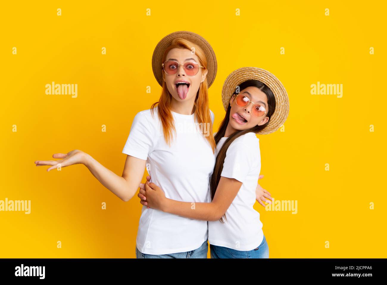 Studio portrait d'enfant drôle avec maman. Visage amusant. Mère et fille adolescente embrassant un joli câlin, portant des t-shirts blancs chapeau paille et Banque D'Images