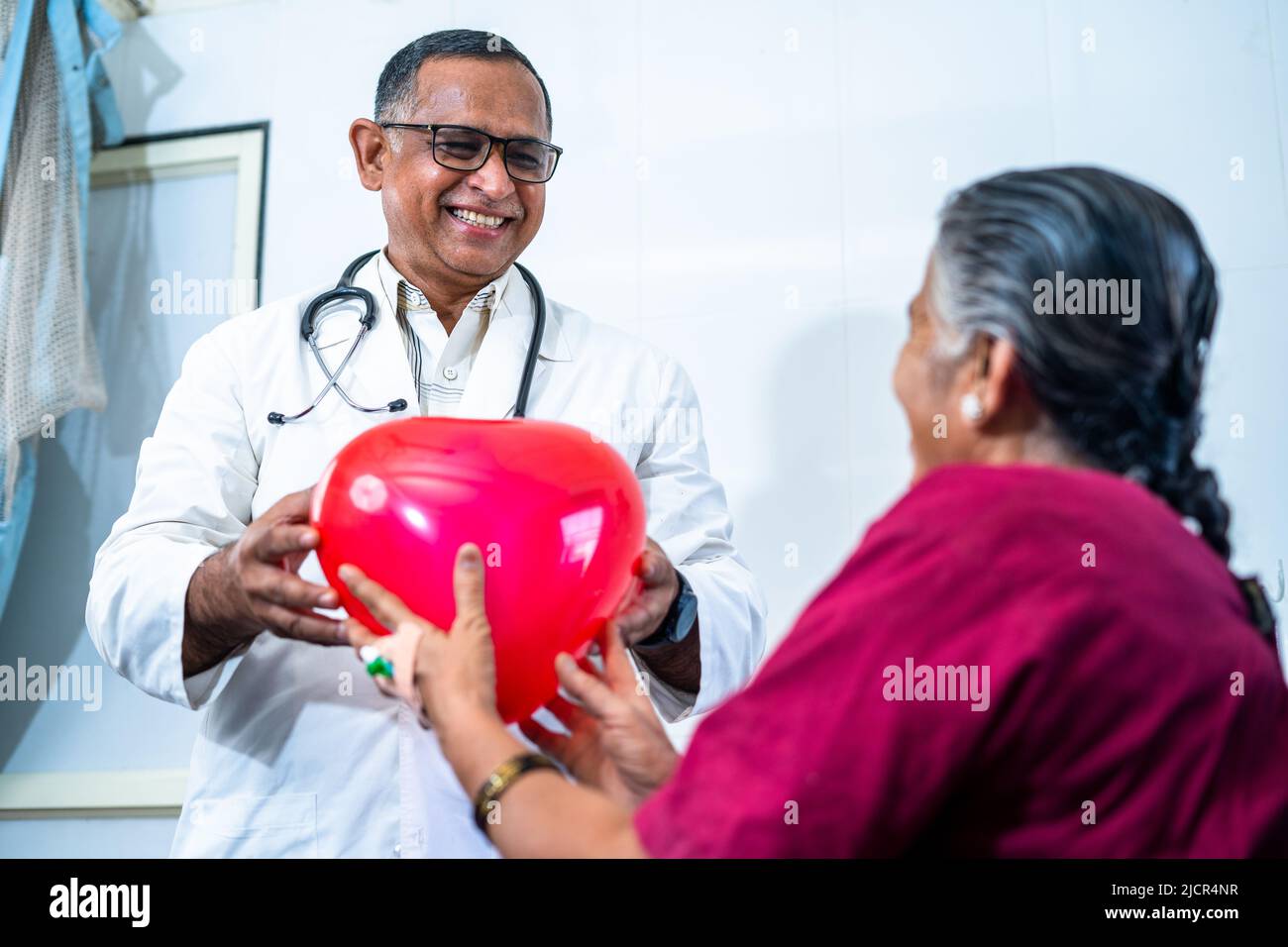 Joyeux sourire médecin donnant le coeur de ballon à un patient âgé retrouvé à l'hôpital - concept de bonheur, de guérison et d'émotion positive. Banque D'Images