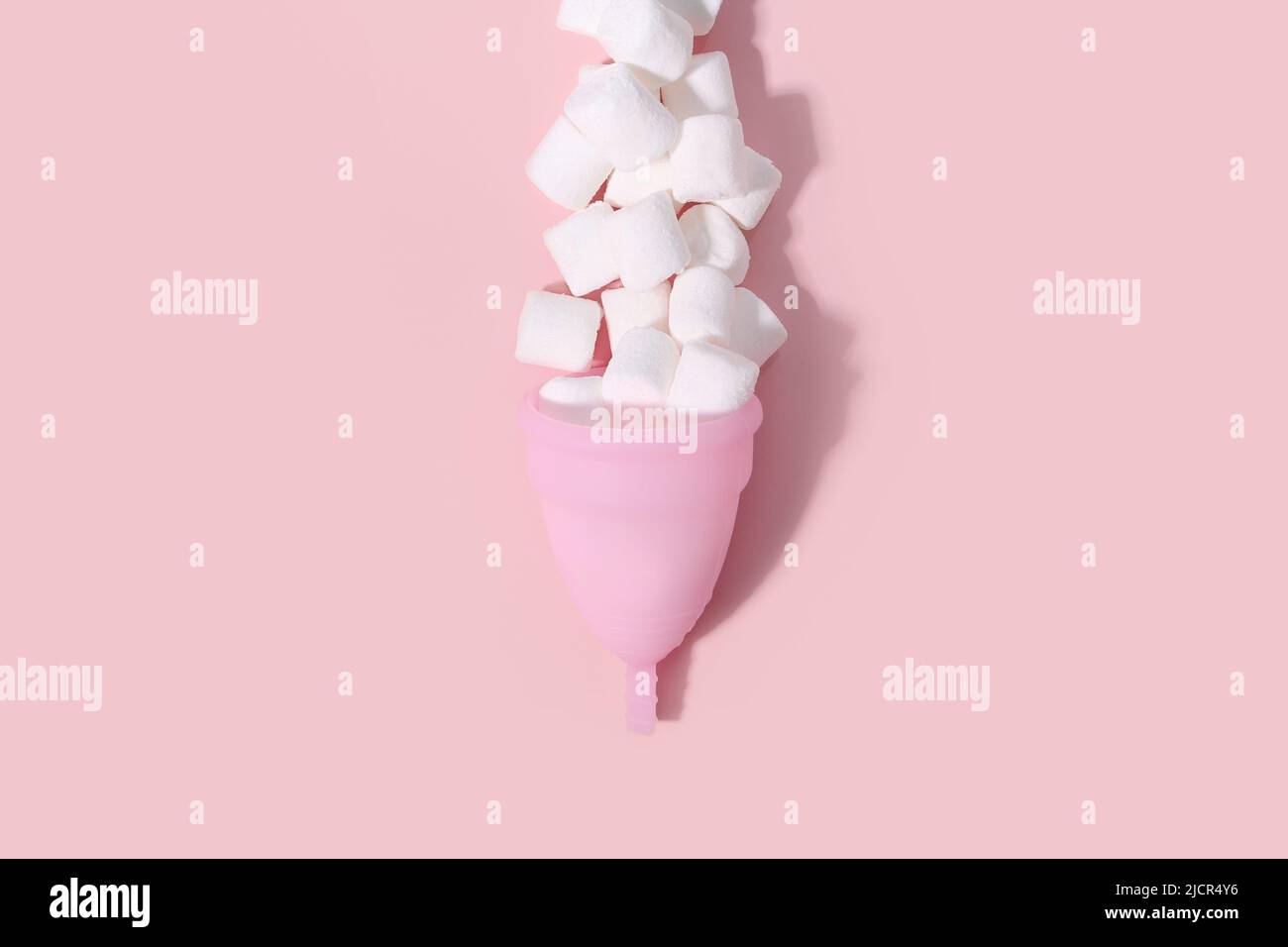 Coupe menstruelle rose et mini guimauve blanche comme une goutte de sang avec ombre sur fond rose. Santé des femmes, hygiène alternative et écologie de l'avion Banque D'Images