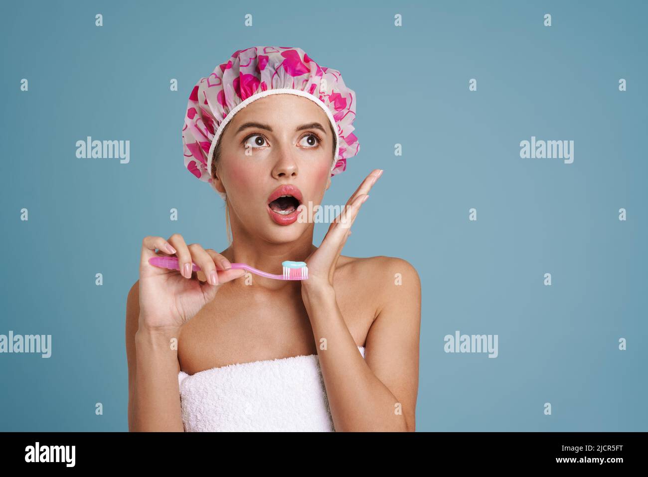 Jeune femme exprimant la surprise tout en se brossant les dents isolées sur le mur bleu Banque D'Images