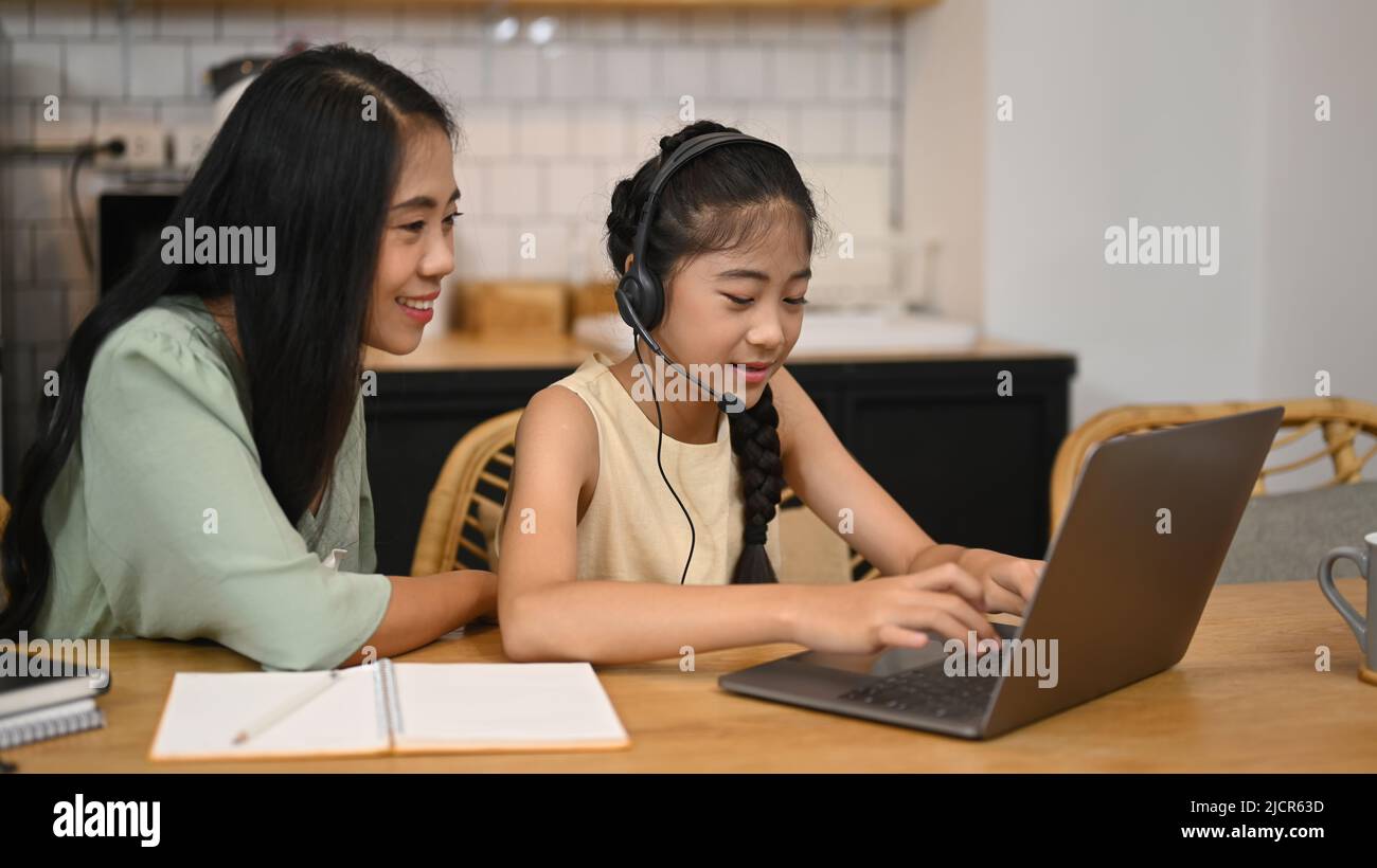 Mère asiatique aidant sa fille à faire ses devoirs, apprenant en ligne à la table de cuisine Banque D'Images