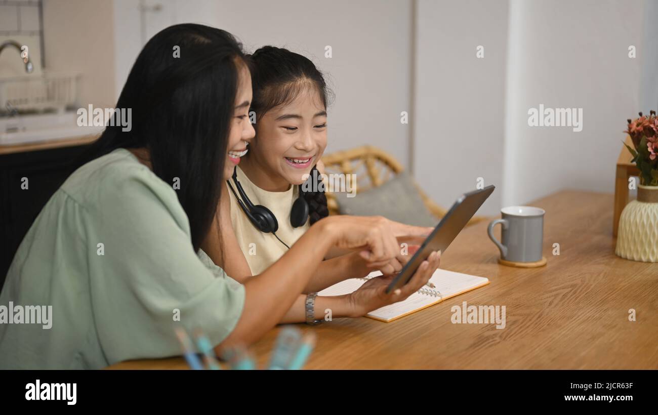 Jeune fille souriante assise avec la mère dans la cuisine et ayant l'apprentissage en ligne à la classe virtuelle. Concept de l'éducation virtuelle, homeschooling Banque D'Images