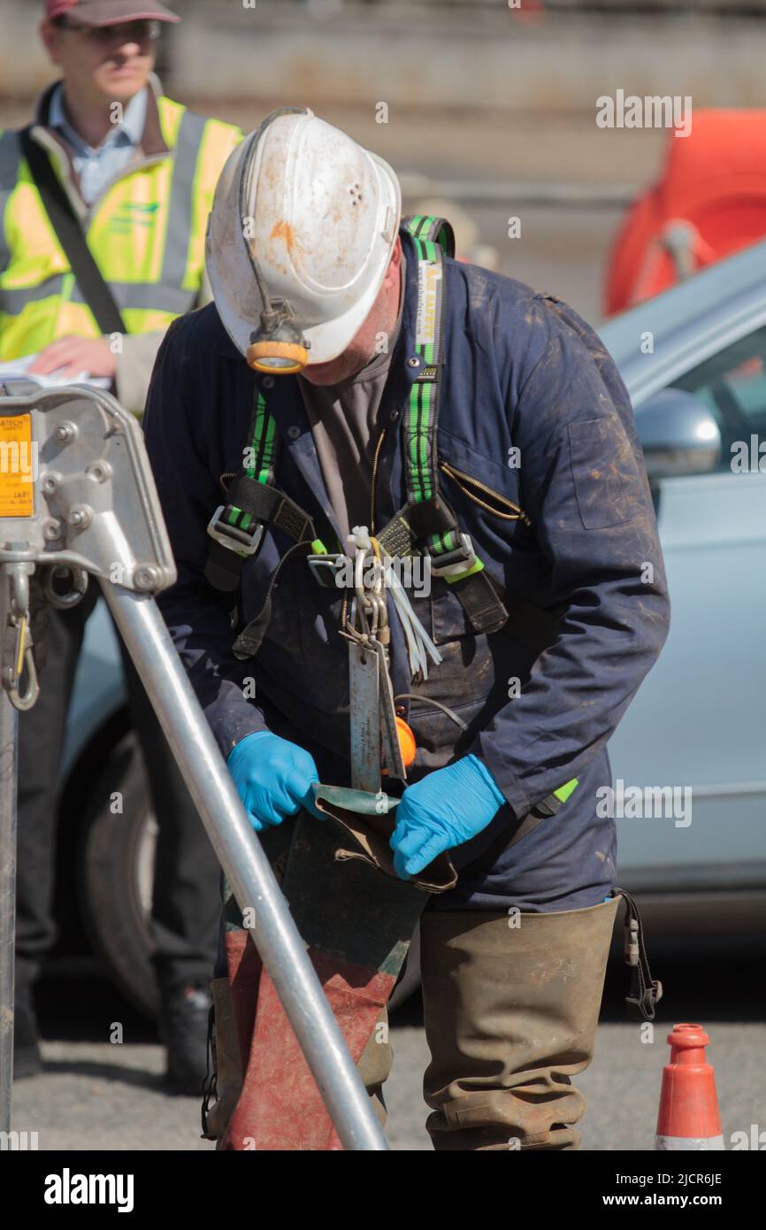 Les travailleurs de Porthleven qui travaillent à la fixation de la conduite d'égout. Un travailleur est hissé dans l'égout sur un cadre de trépied Banque D'Images