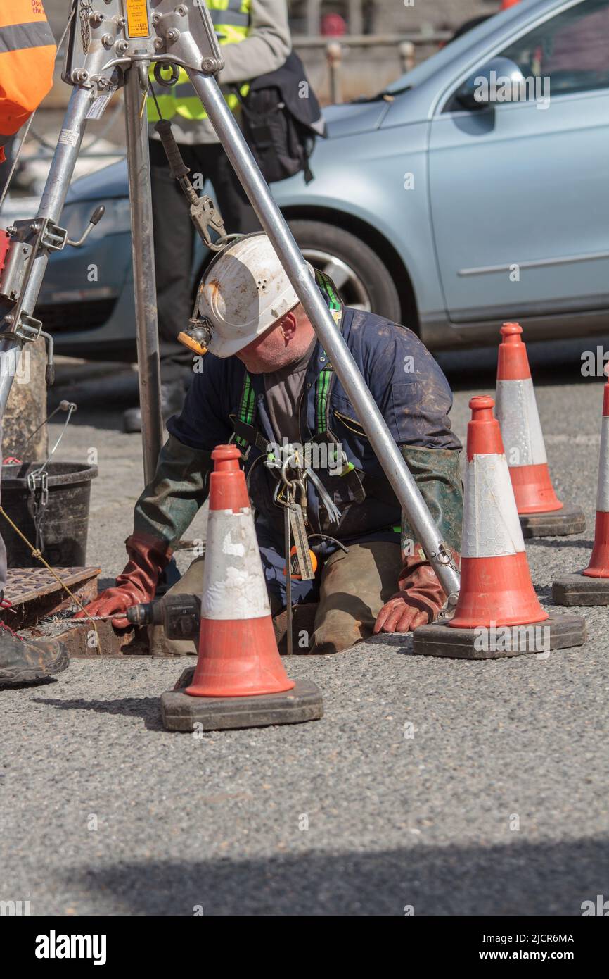 Les travailleurs de Porthleven qui travaillent à la fixation de la conduite d'égout. Un travailleur est hissé dans l'égout sur un cadre de trépied Banque D'Images