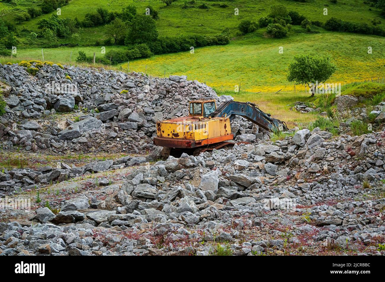 Des tas de blocs de calcaire et un vieux creuseur à 360° rouillé dans une carrière abandonnée sur un ancien site minier près de Bradwell, Peak District. Banque D'Images