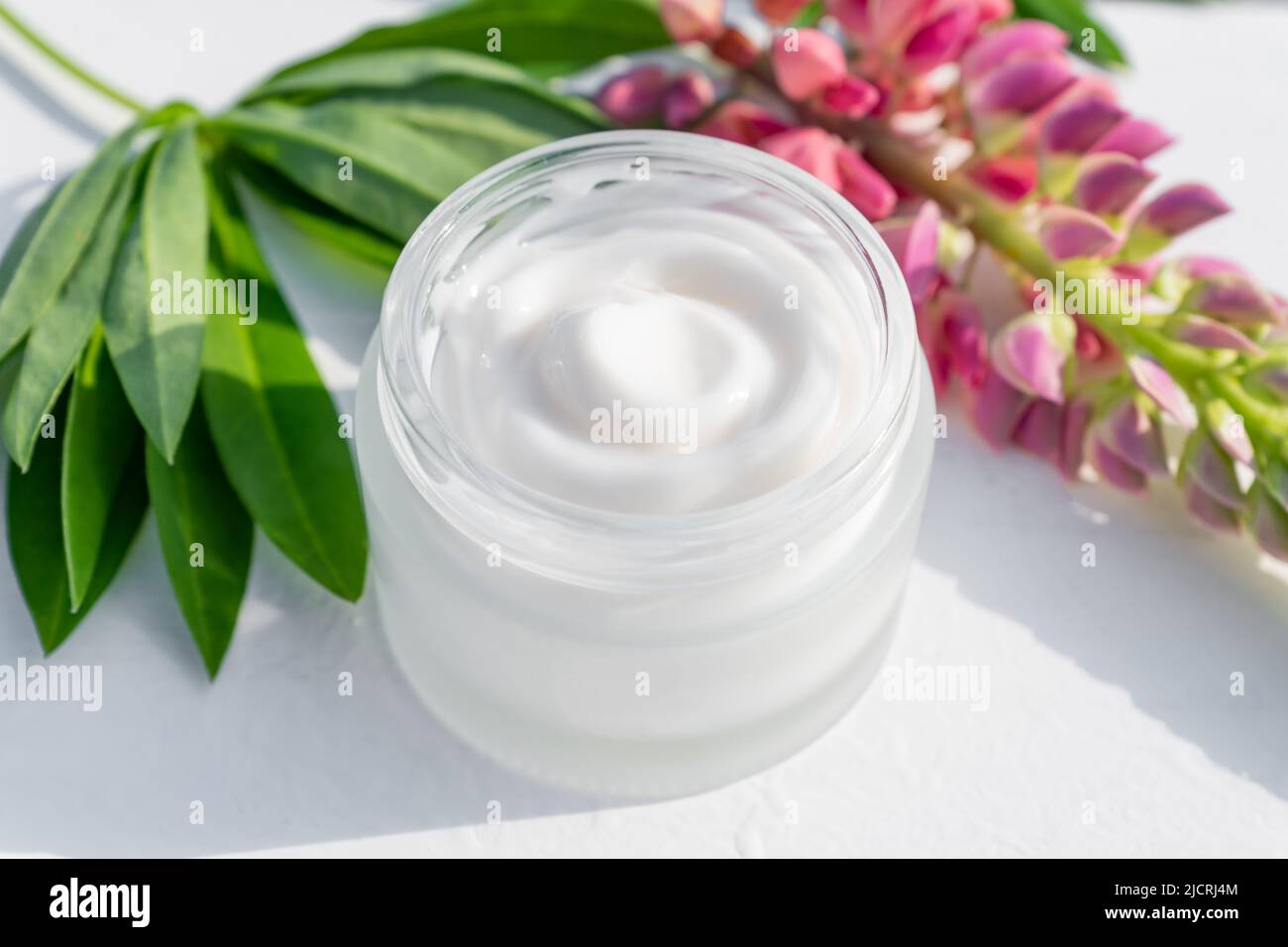 Jarre blanche sans marque et fleurs de lupins roses sur fond de table en bois. Bouteille pour marquage et étiquette. Cosmétiques naturels bio spa. Copier l'espace Banque D'Images