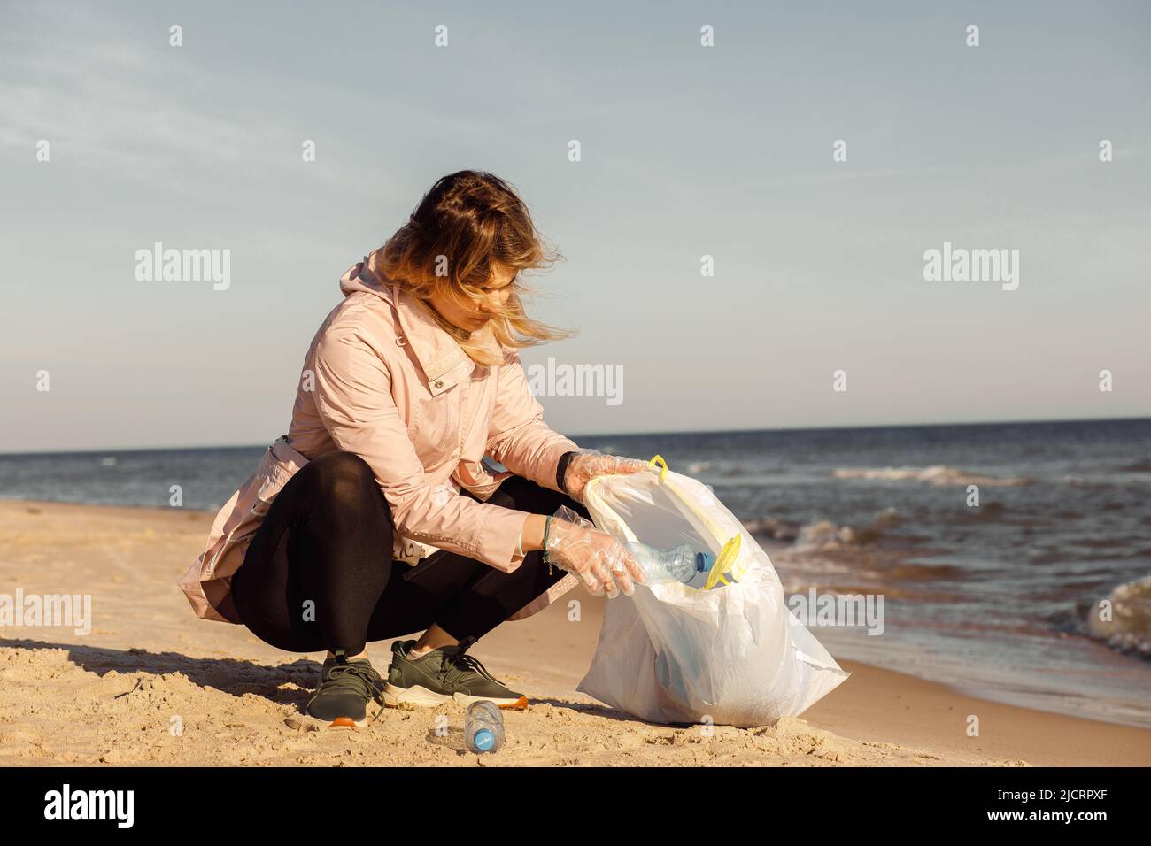 Femme activiste et assistante nettoyant la plage de sable des déchets sous-marins, de la mer ou de l'océan avec des déchets de plastique. Changement global. Banque D'Images