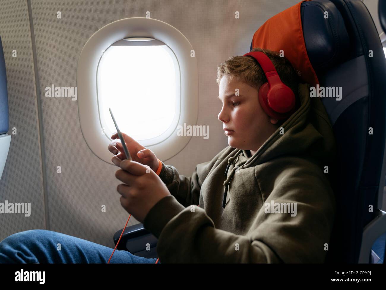 Un garçon de 11 ans vole dans un avion et joue sur une tablette. Banque D'Images