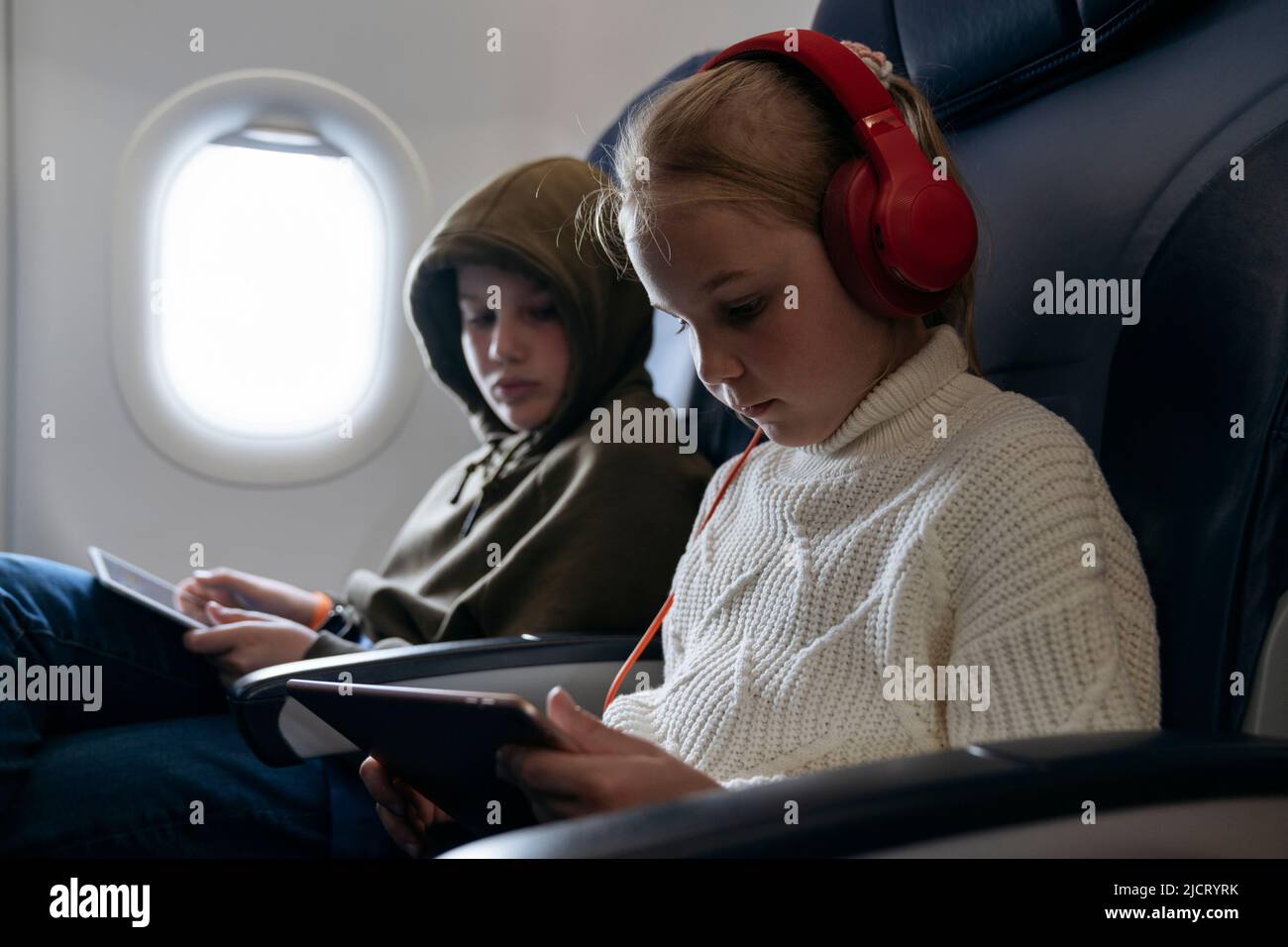 Les enfants volent dans un avion et regardent une tablette. Banque D'Images