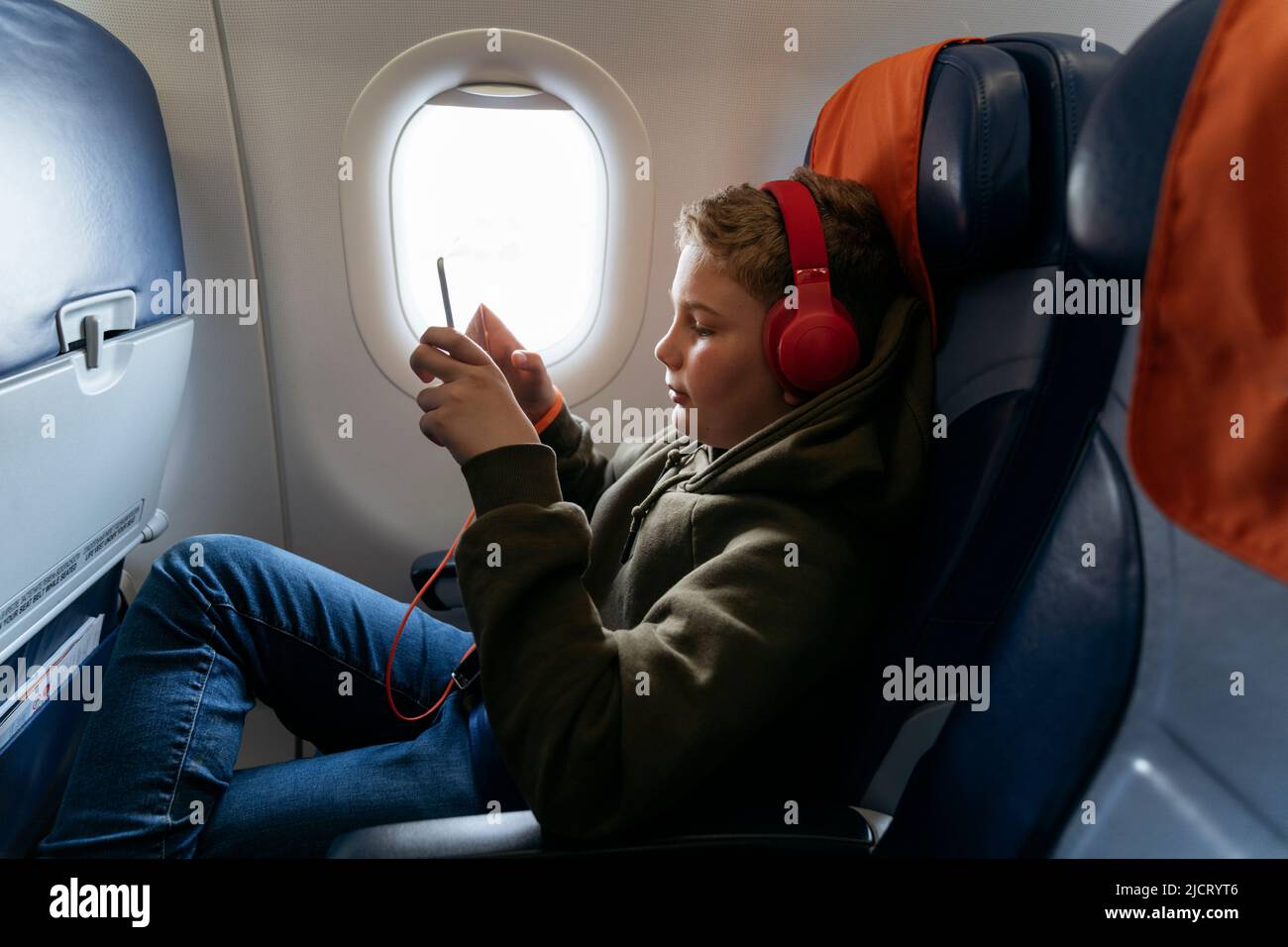 Un garçon vole dans un avion avec un casque et joue sur une tablette. Banque D'Images