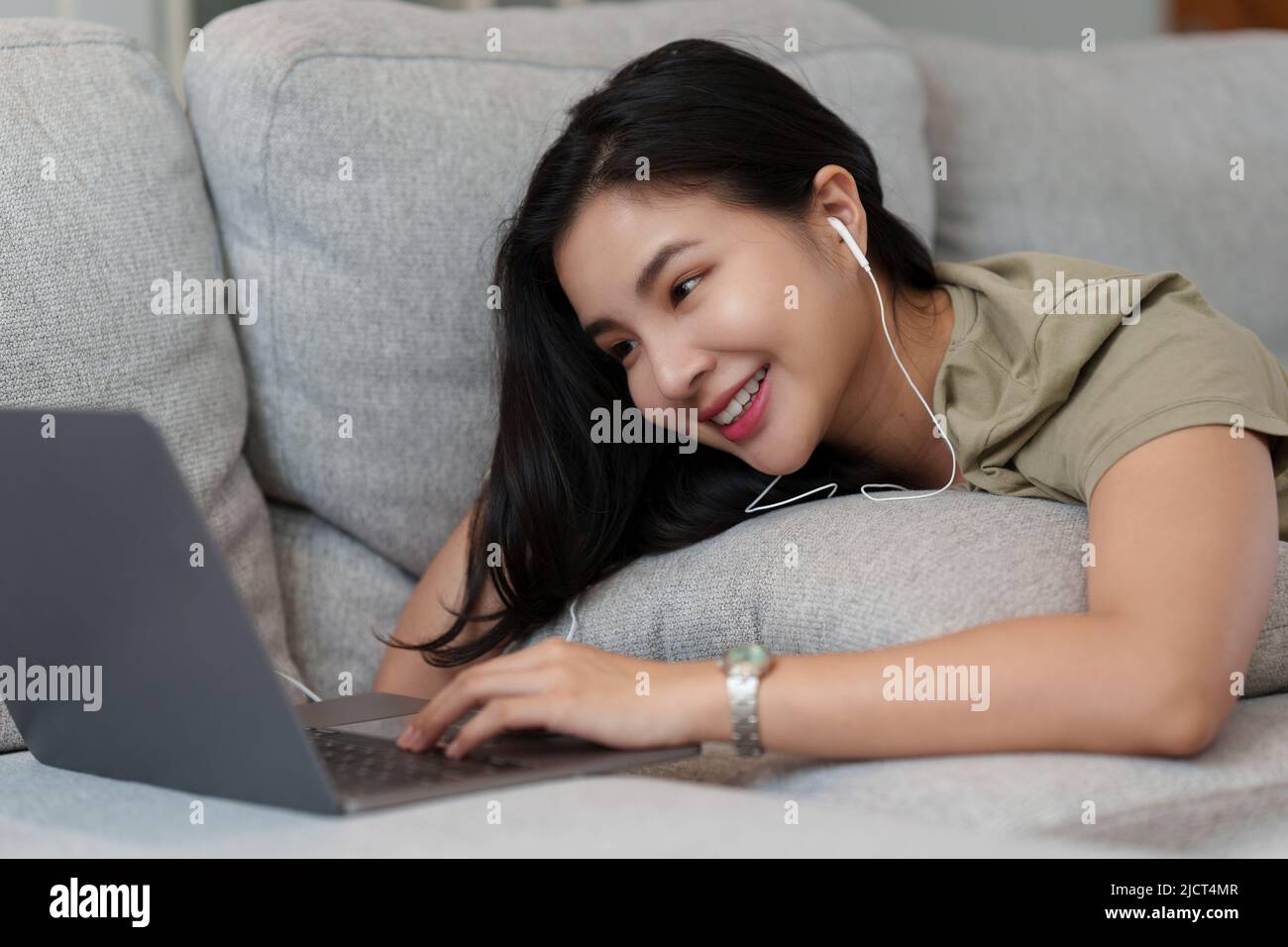 Portrait d'une femme heureuse et belle couché sur un canapé confortable et écouter de la musique en streaming sur un ordinateur portable. Banque D'Images