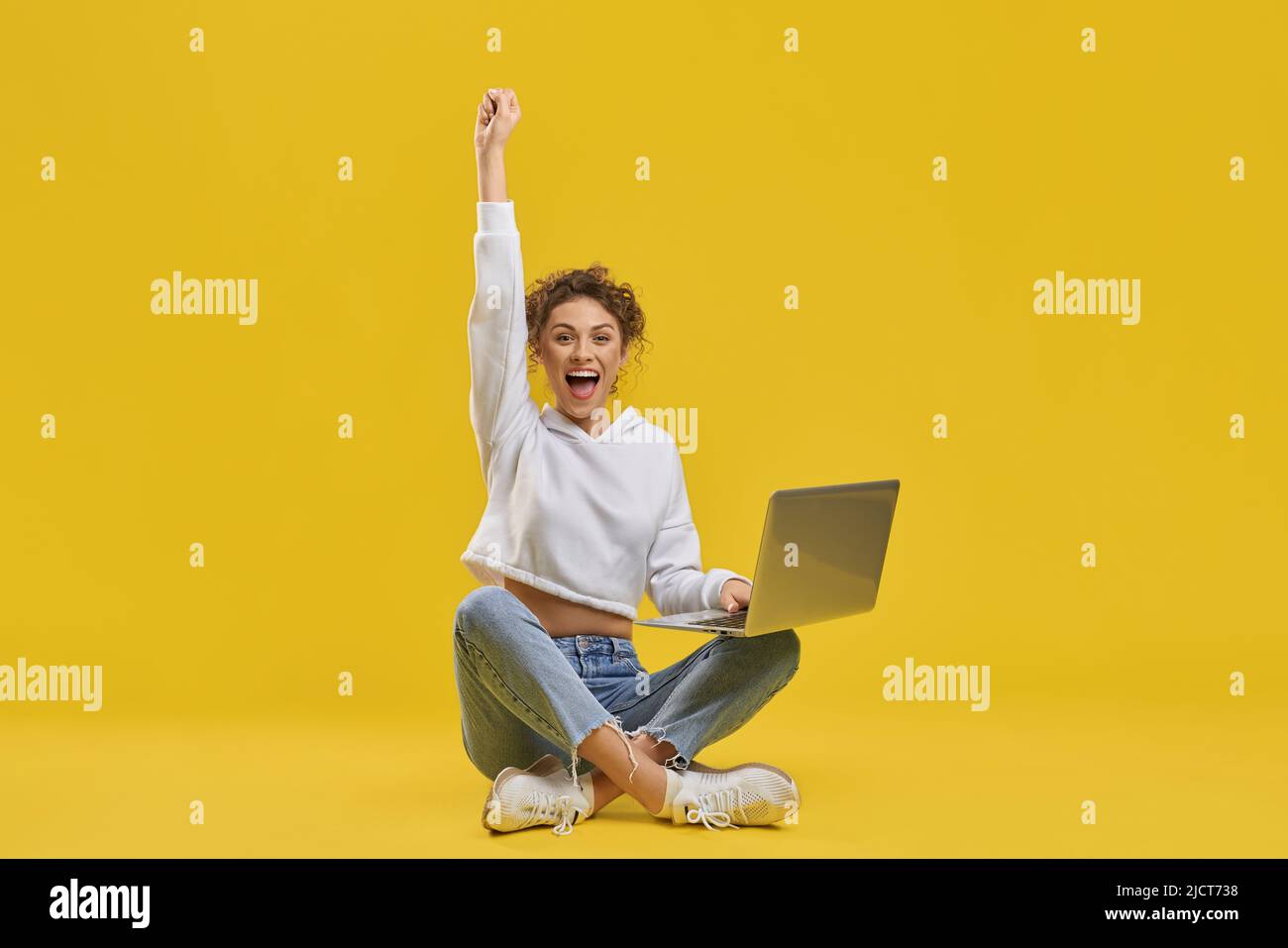 Une femme excitée célébrant la victoire, regardant l'écran du netbook à l'intérieur. Vue de face d'une femme freelance heureuse appréciant un démarrage réussi, levant la main, isolée sur fond orange. Concept d'émotion. Banque D'Images