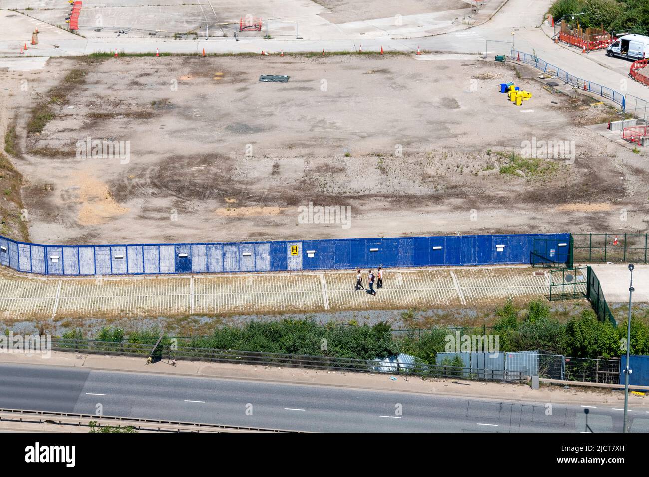 Prise de vue aérienne pendant que 3 personnes marchent devant un site de construction vide dans les Docklands de l'est de Londres. Banque D'Images