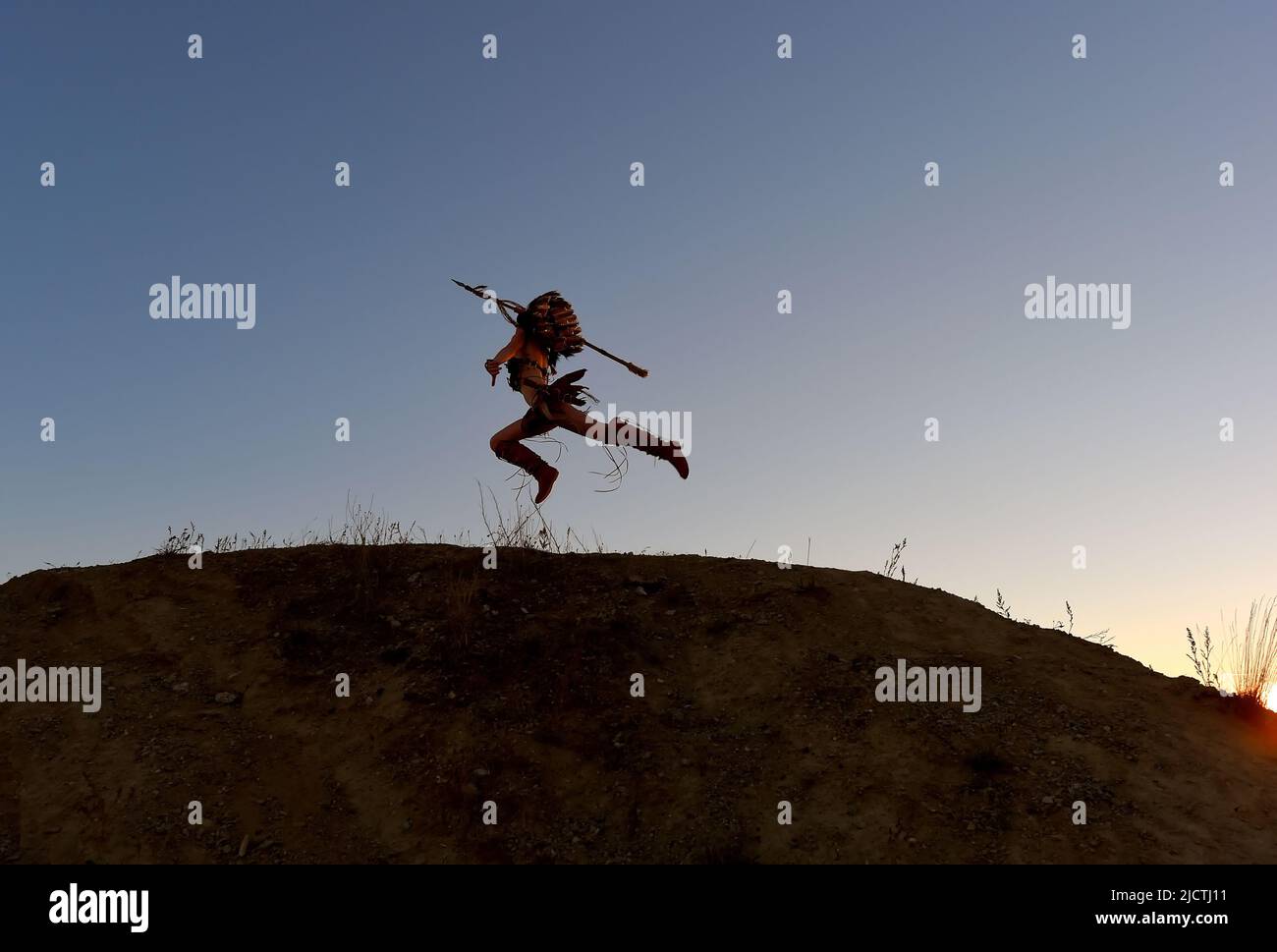 Une jeune fille est silhouettée comme indienne d'origine américaine. Elle est vue courir et charger une colline au soleil avec une lance dans sa main. Banque D'Images