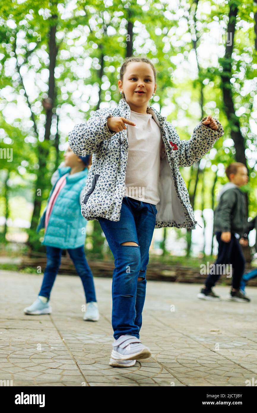 Petite fille fraîche marchant avec d'autres enfants dans l'aire de jeux dans le parc vert. Vacances d'été dans le camp, centre touristique. Marcher et jouer à l'extérieur, sport Banque D'Images