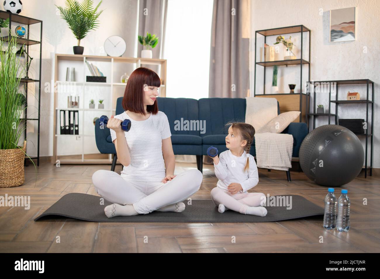 Sport, concept d'entraînement. Maman et petite fille faisant des exercices  de haltères sur un tapis de yoga dans le salon à la maison. Nouveau concept  normal. Un mode de vie sain. Détente