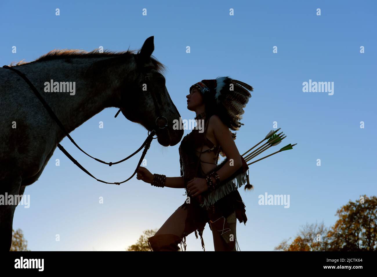 Une jeune fille est vue au coucher du soleil comme un Indien amérindien. Elle est vue avec son cheval comme le soleil se met dans la distance. Banque D'Images