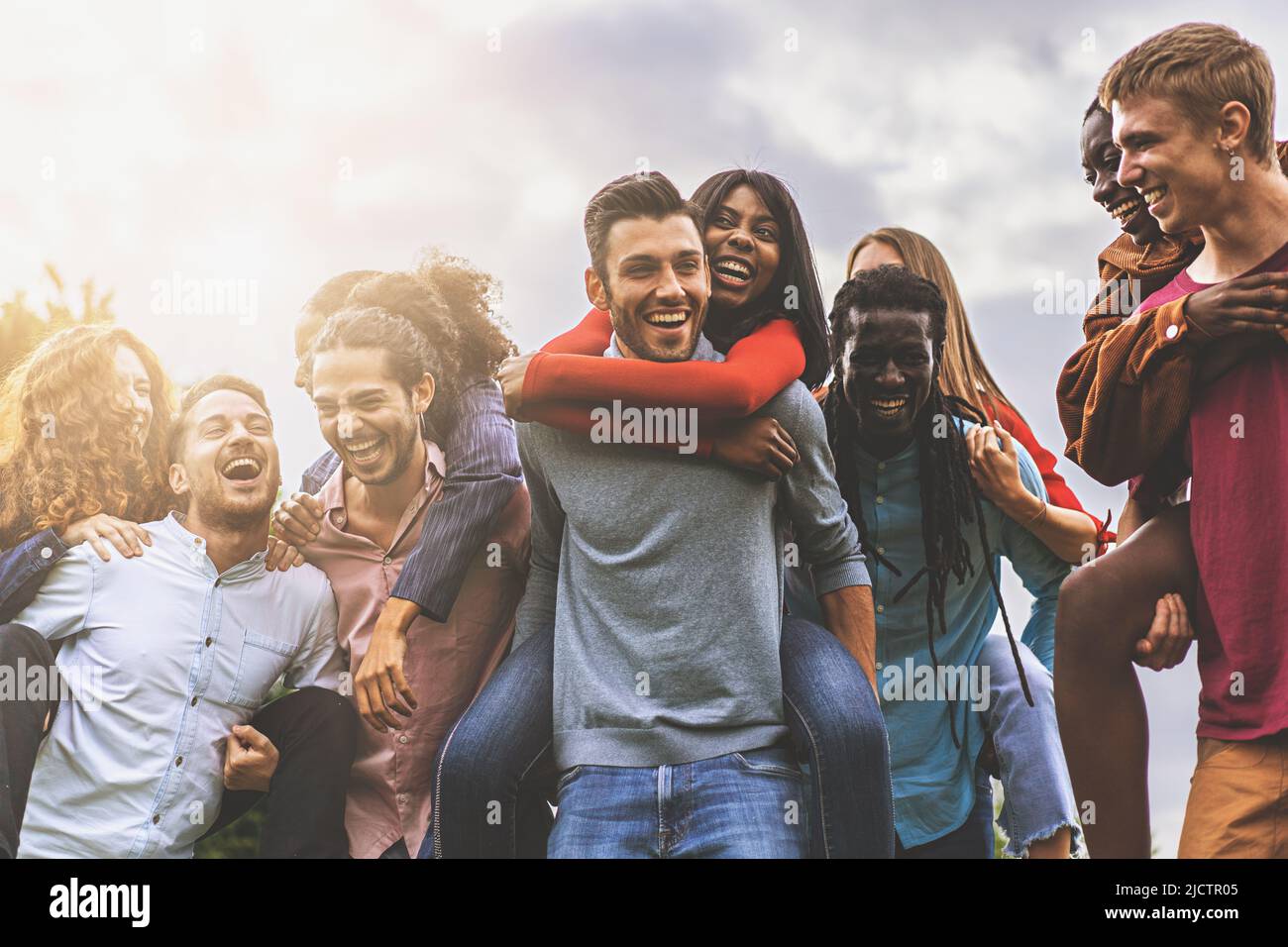 Groupe de jeunes amis de différentes races et cultures ont l'amusement insouciant de jouer le piggyback ensemble à l'extérieur - concept de vie de culture de jeunesse Banque D'Images