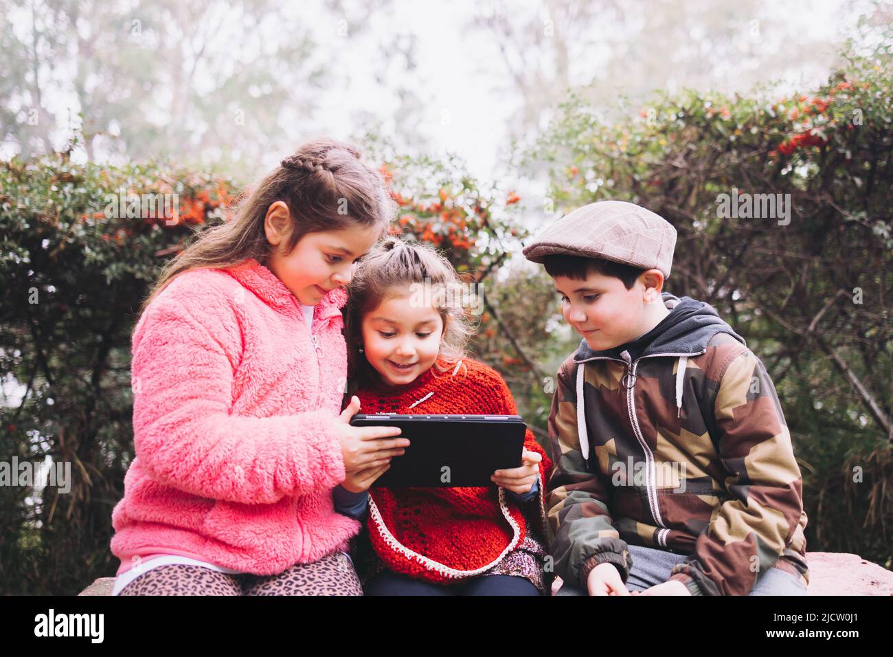Deux filles et un garçon utilisant une tablette pour regarder un film, dans le parc. Les enfants latins Banque D'Images