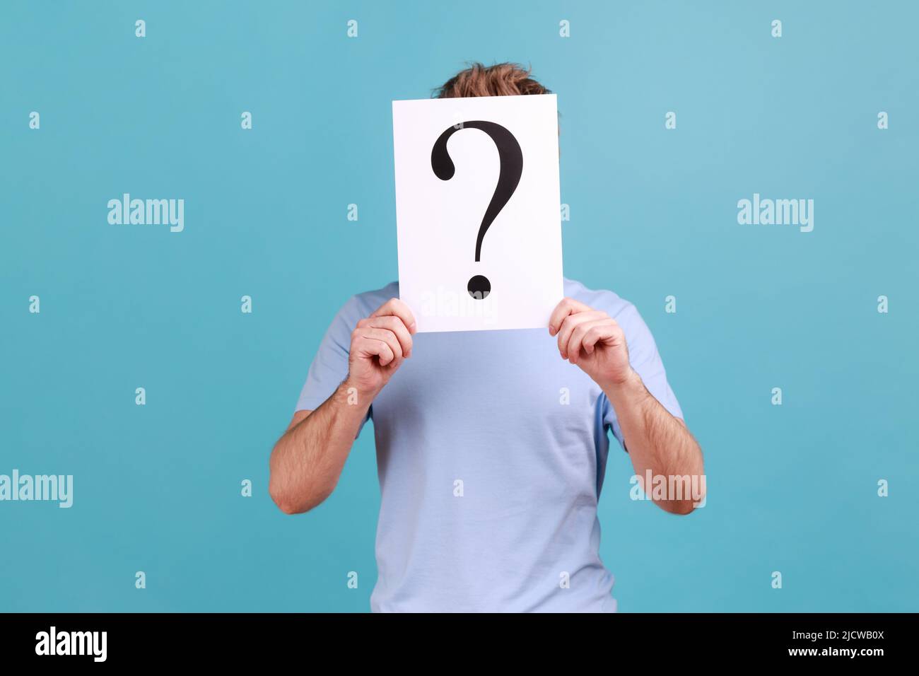 Portrait d'un homme barbu inconnu qui cache son visage derrière un livre blanc avec un point d'interrogation, qui trouve une solution intelligente et demande des conseils. Studio d'intérieur isolé sur fond bleu. Banque D'Images
