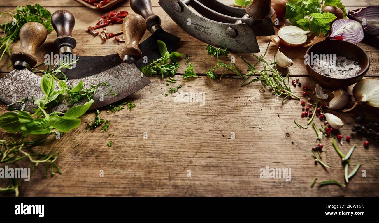 De dessus des couteaux traditionnels mezzaluna sur table en bois avec des herbes vertes fraîches et divers arômes dans la cuisine légère Banque D'Images