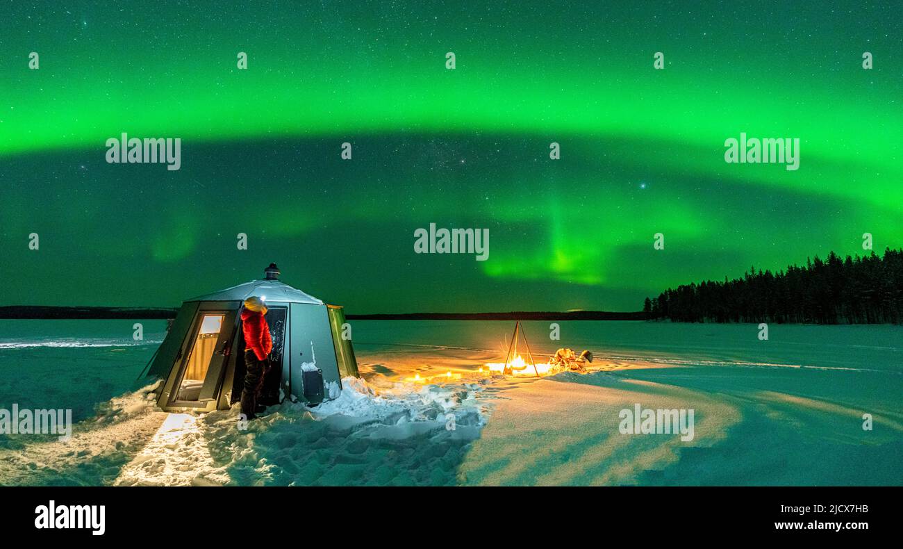 Randonneur regardant l'Aurora Borealis (aurores boréales) près du feu de camp et de l'igloo dans le paysage gelé, Jokkmokk, Laponie, Suède, Scandinavie Banque D'Images