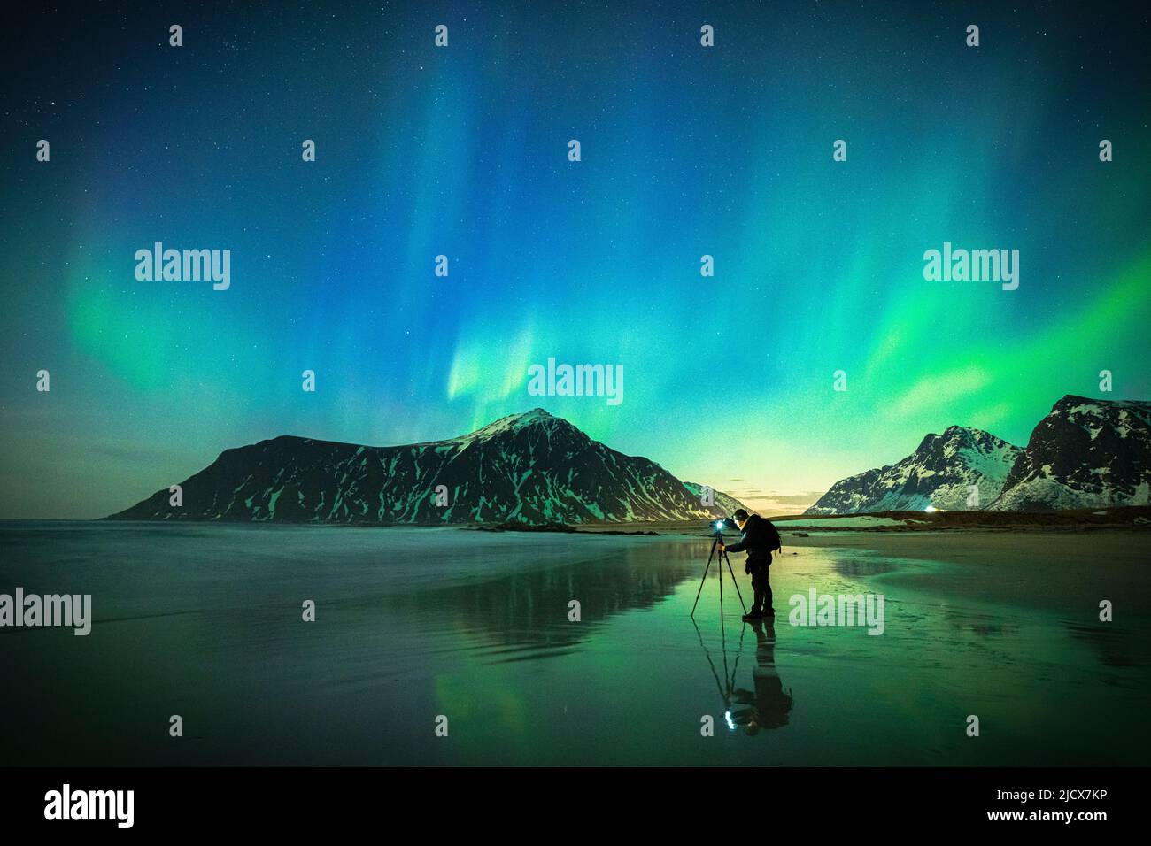 Personne photographiant le ciel lumineux pendant l'aurore Borealis (aurores boréales) debout sur la plage de Skagsanden, îles Lofoten, Norvège, Scandinavie Banque D'Images