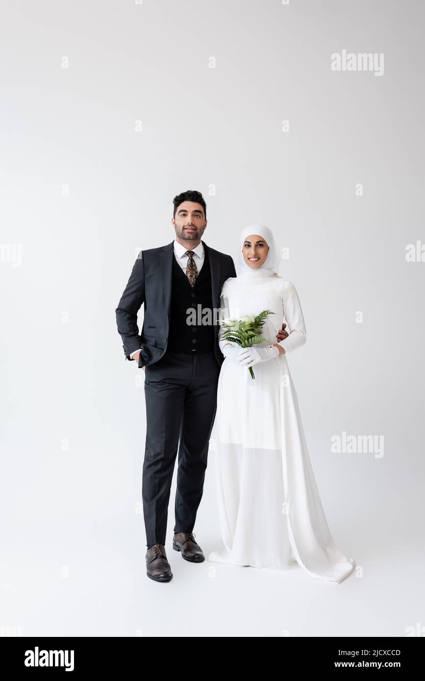 bonne mariée musulmane en gants et robe de mariage tenant bouquet près de  marié en costume sur gris Photo Stock - Alamy
