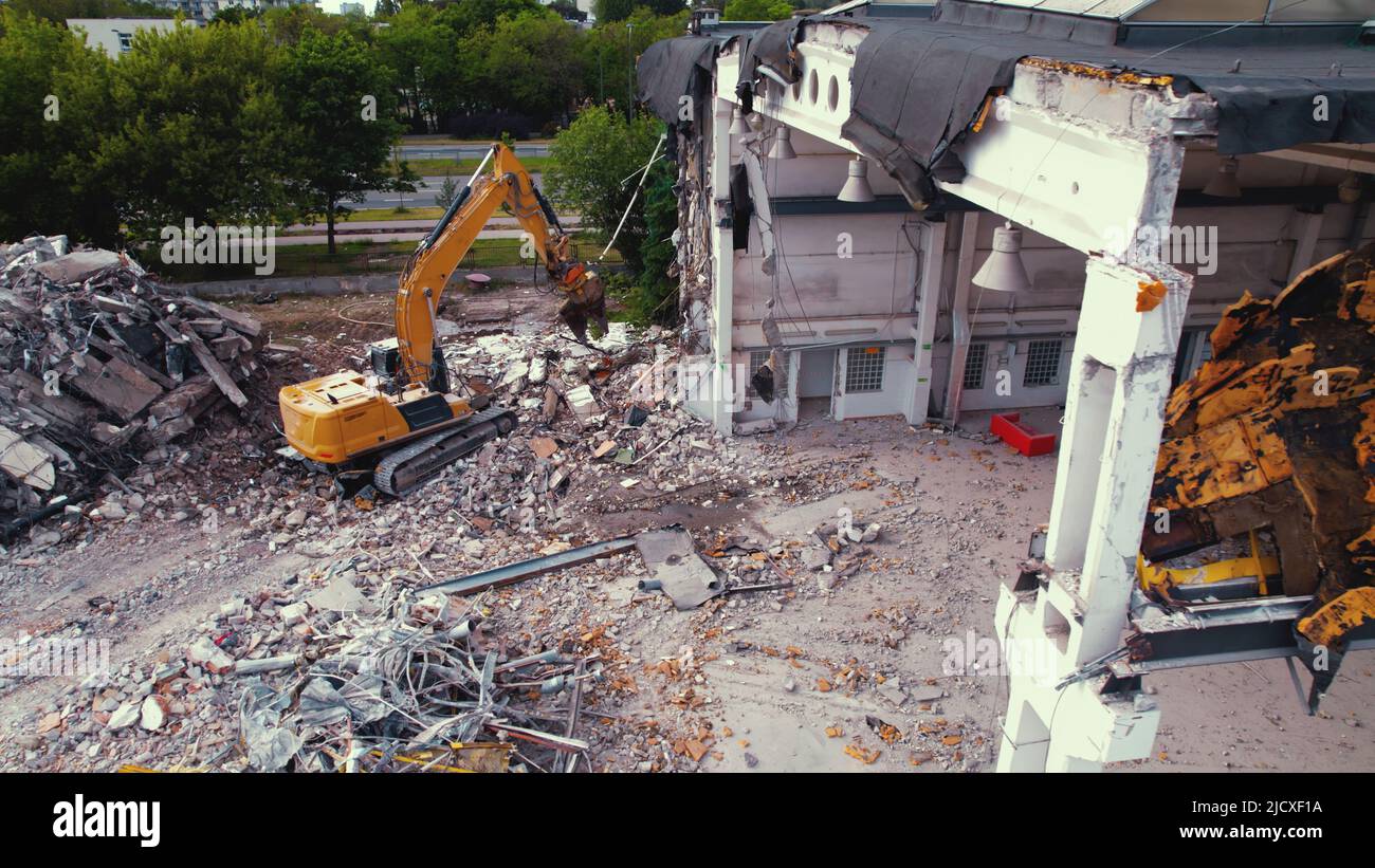 Un grand creuseur jaune démolissant un grand vieux bâtiment blanc laissant beaucoup de débris autour du site. Photo de haute qualité Banque D'Images