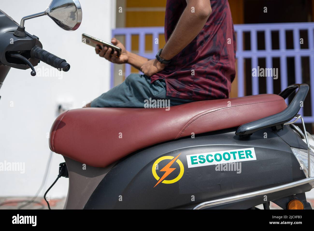 Jeune homme utilisant le téléphone portable près du point de charge pendant la recharge de ev ou de scooter électrique - concept de écologique, renouvelable et zéro émission Banque D'Images