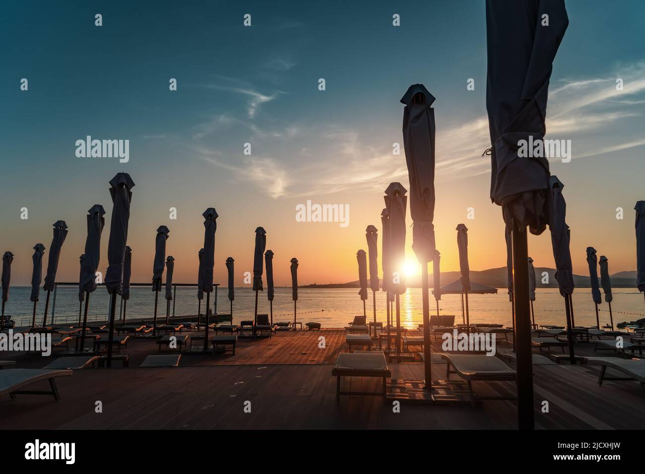 Coucher de soleil sur la plage de la station avec chaises longues et parasols roulés. Banque D'Images