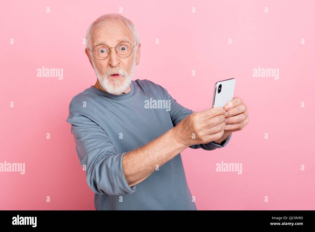 Photo de impressionné funky Guy retraité habillé gris pull-over verres écriture dispositif moderne isolé couleur rose fond Banque D'Images