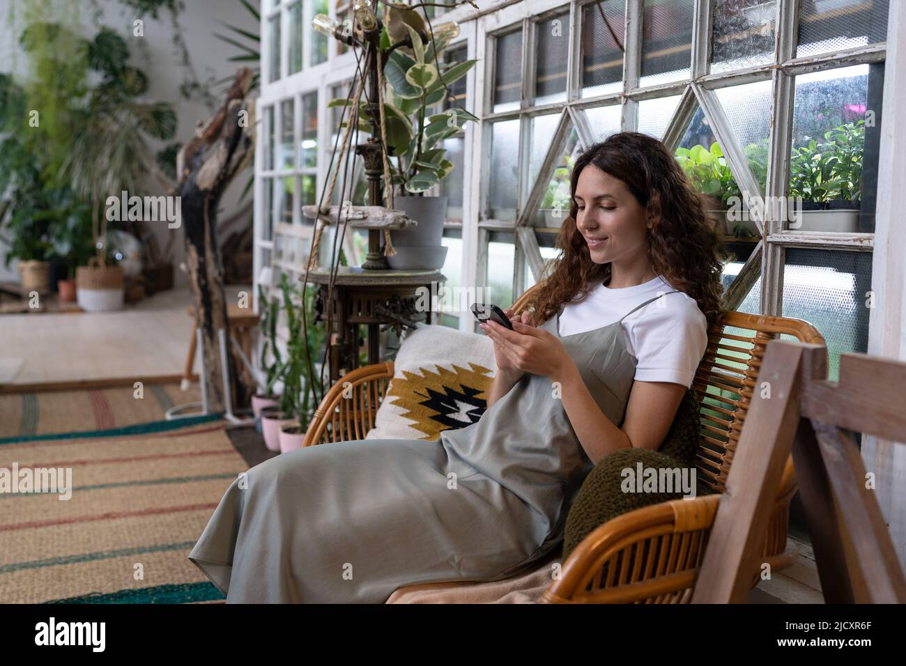 Une femme souriante se détendre dans le jardin à la maison à l'aide d'un smartphone, en discutant sur les réseaux sociaux avec un ami Banque D'Images