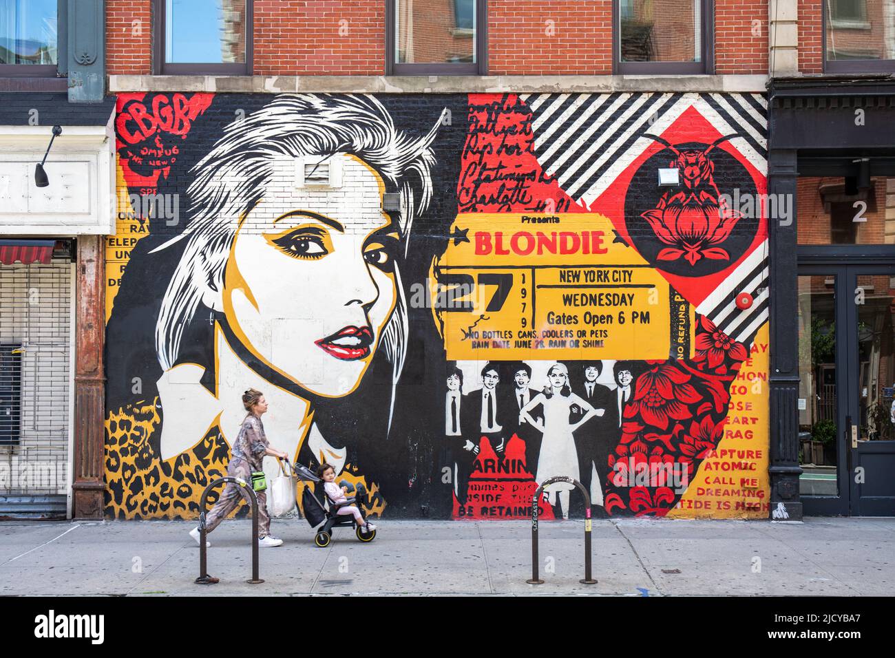 Femme avec un enfant dans une poussette passant la fresque de Blondie par Shepard Fairey dans Bleecker Street, Lower East Side de Manhattan à New York City, Etats-Unis Banque D'Images