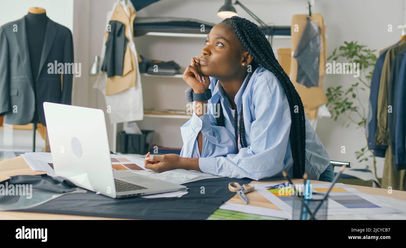 Un talentueux designer de mode afro-américain crée une nouvelle collection de mode tout en travaillant sur un ordinateur portable dans un studio Fashion Business Startup. Concept Banque D'Images