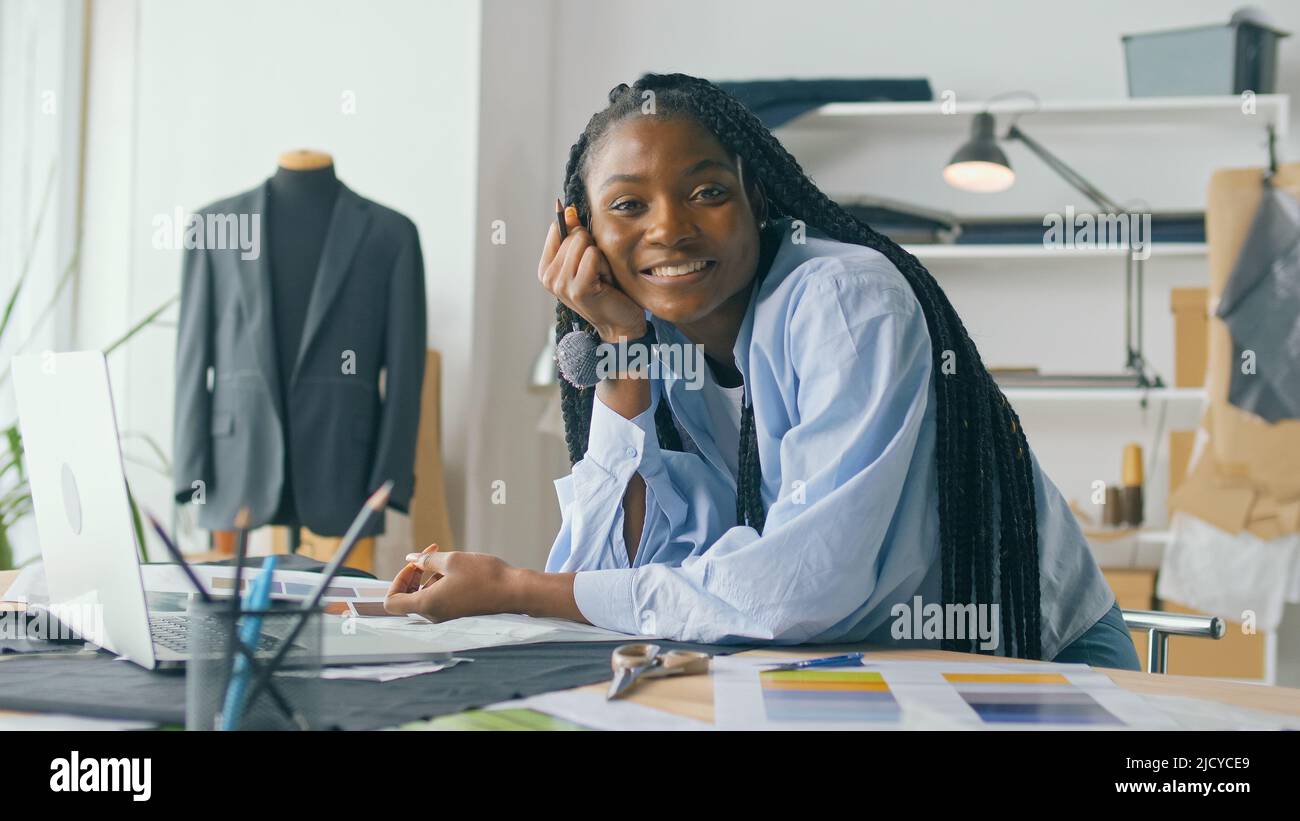 Un talentueux designer de mode afro-américain crée une nouvelle collection de mode tout en travaillant sur un ordinateur portable dans un studio Fashion Business Startup. Concept Banque D'Images