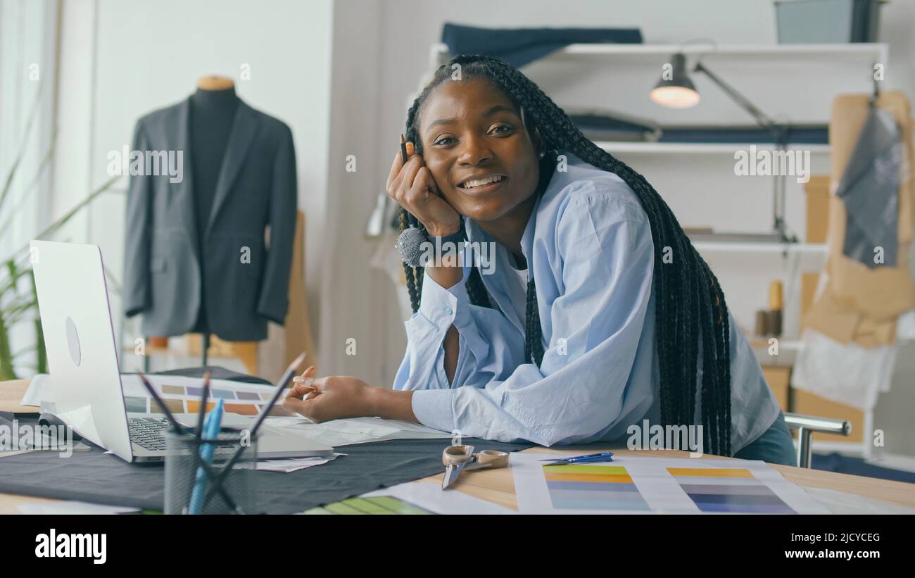 Un talentueux designer de mode afro-américain crée une nouvelle collection de mode tout en travaillant sur un ordinateur portable dans un studio Fashion Business Startup. Concept Banque D'Images
