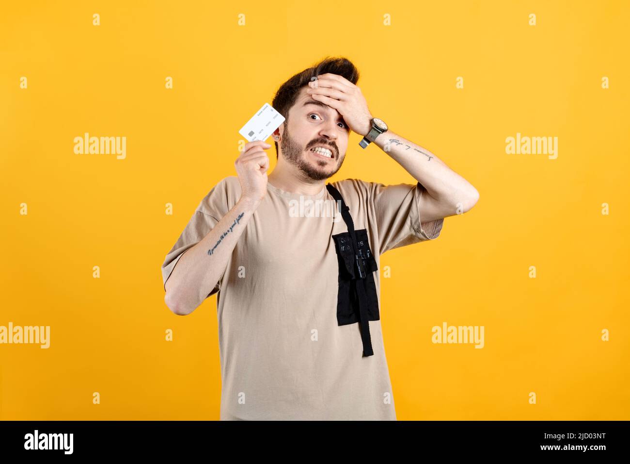 Homme caucasien portant le tee beige posant isolé sur fond jaune montrant la carte de crédit stressée avec la main sur la tête, choqué par la honte et la surprise Banque D'Images