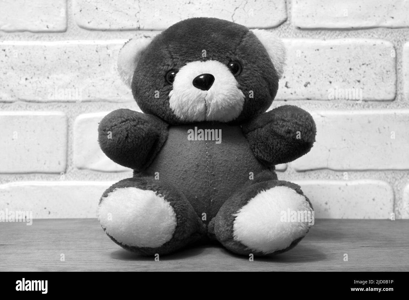 Photo noir et blanc d'un ours en peluche. Ours en peluche sur une table en bois contre un mur de briques Banque D'Images