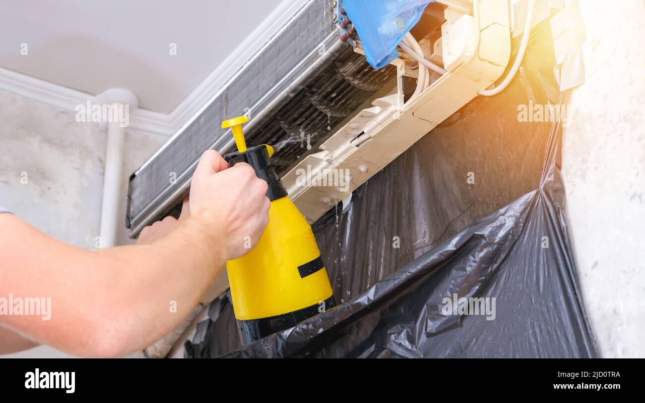 Un homme lave une mousse spéciale pour nettoyer les climatiseurs avec un jet d'eau sous pression. Maintenance du système divisé. Banque D'Images