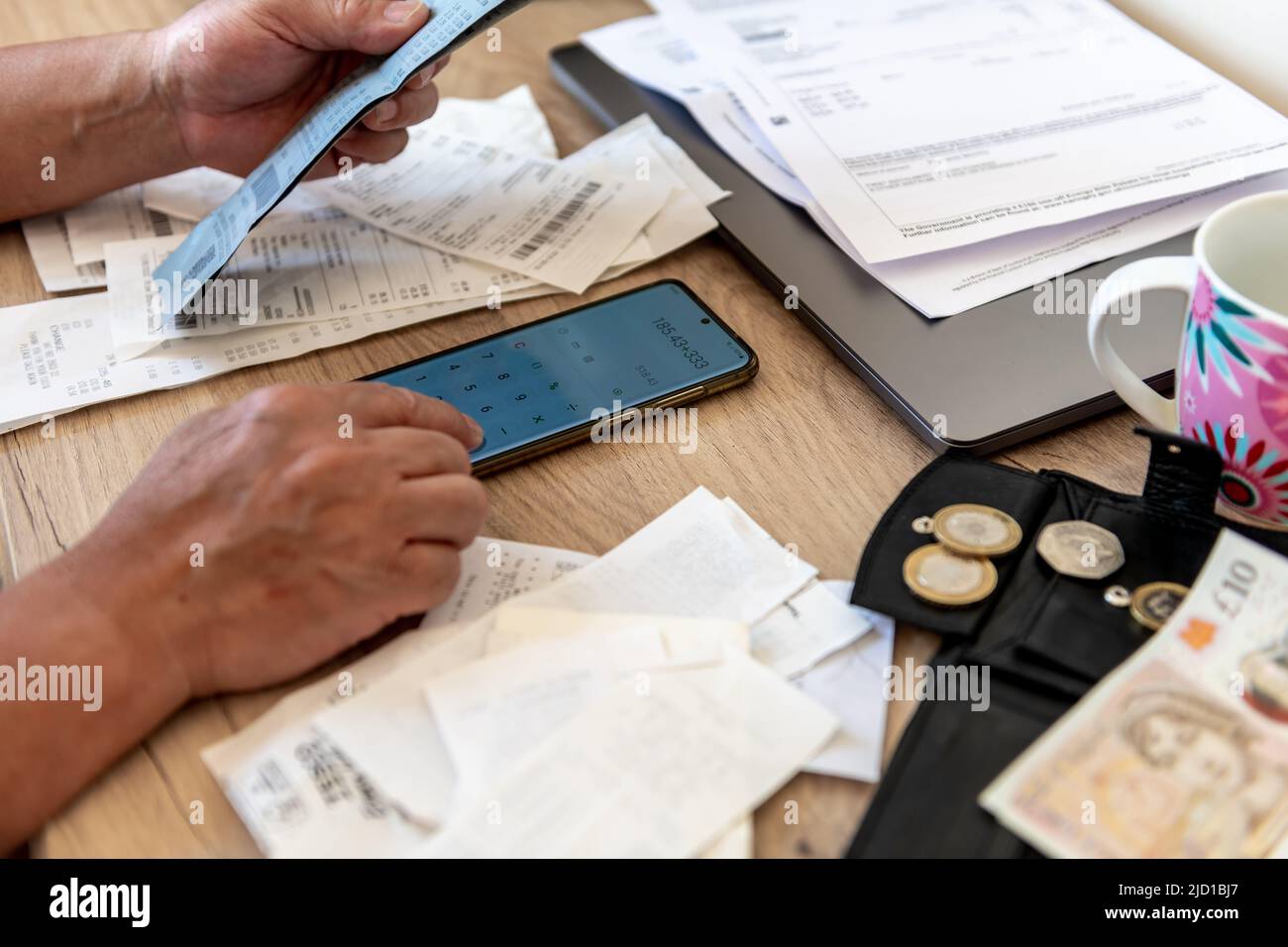 Une personne calculant le coût de la vie avec une calculatrice téléphonique et un bureau rempli de factures et de reçus de caisse. Banque D'Images