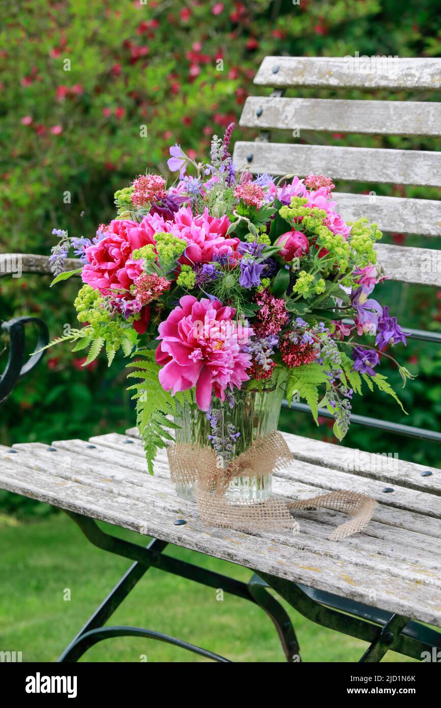 Bouquet coloré dans les tons rouge, rose et violet avec des pivoines et des colonnes, supports en vase de verre sur banc de jardin décoratif en bois Banque D'Images
