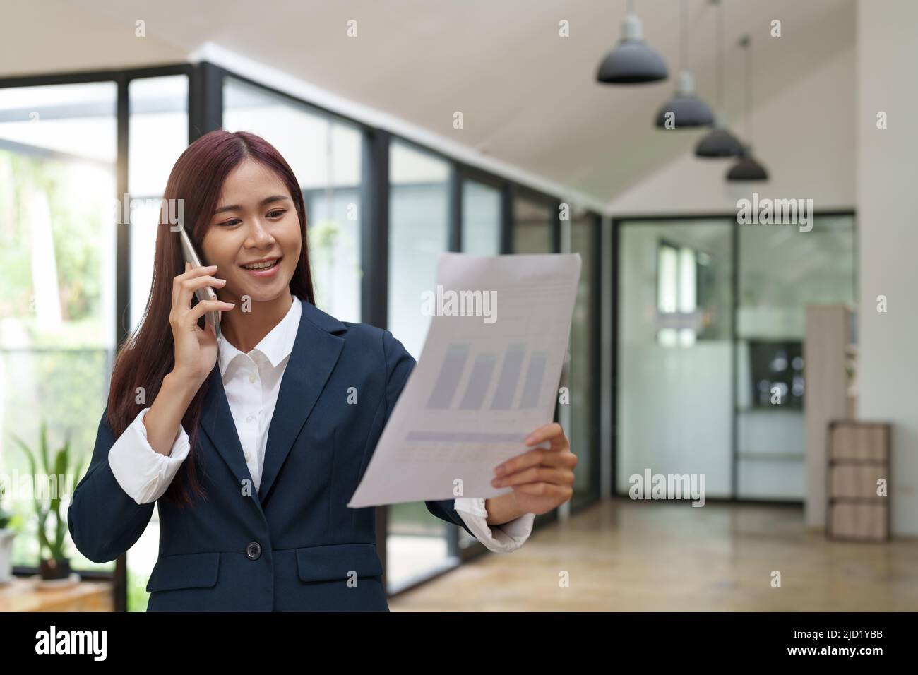 Une jeune femme d'affaires asiatique parle au téléphone portable pour discuter de la paperasse. Banque D'Images