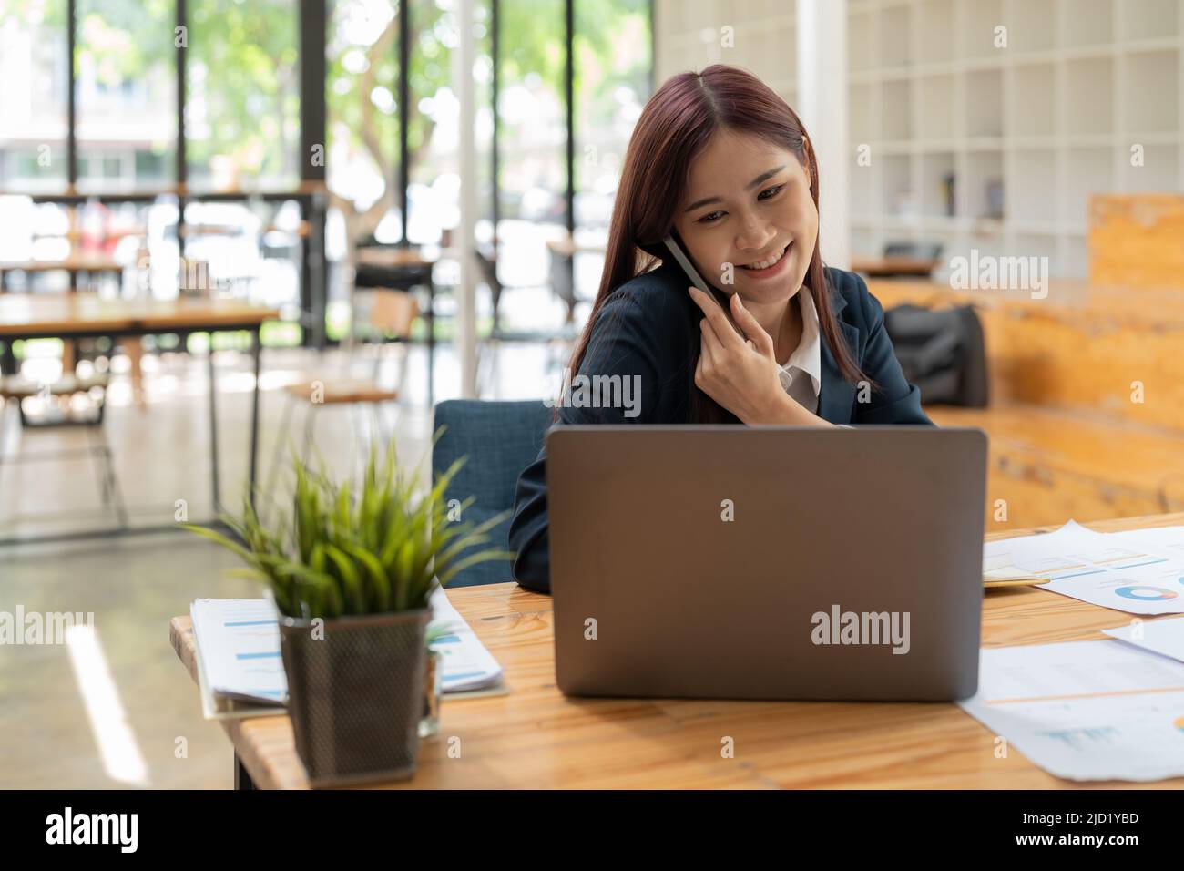 Femme d'affaires asiatique souriante en costume noir parlant au téléphone Banque D'Images