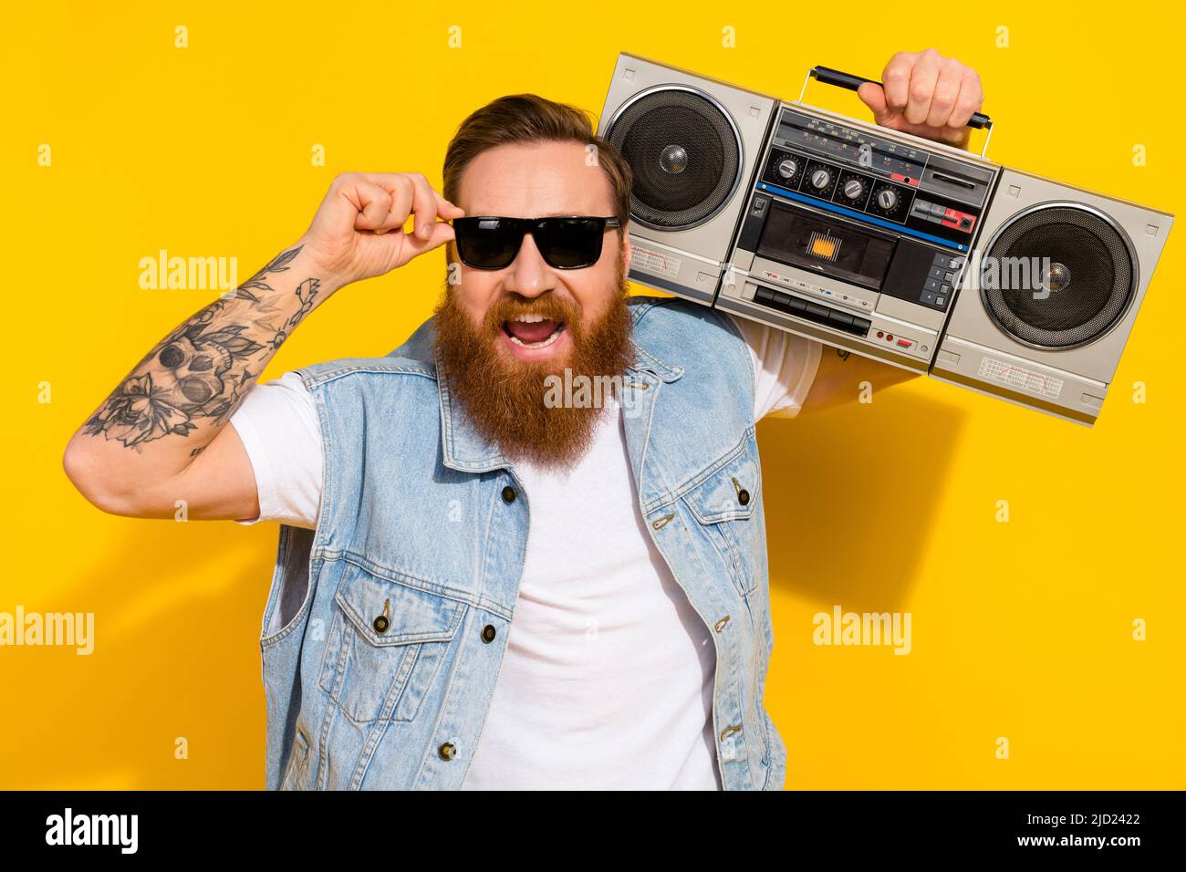 Photo de drôle impressionné gars habillé denim gilet montant verres sombres appréciant des chansons boombox isolé couleur jaune fond Banque D'Images